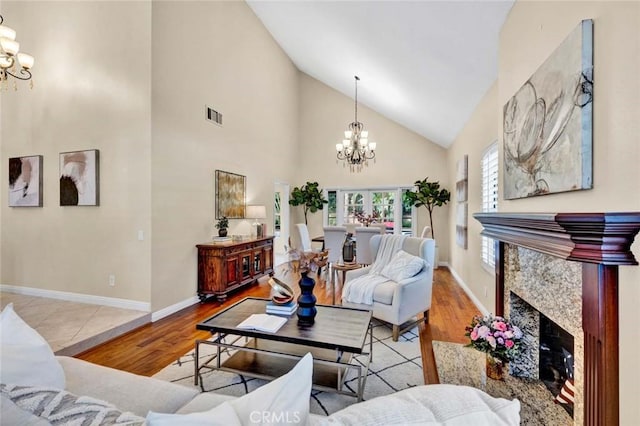 living room with a high end fireplace, high vaulted ceiling, an inviting chandelier, and light wood-type flooring