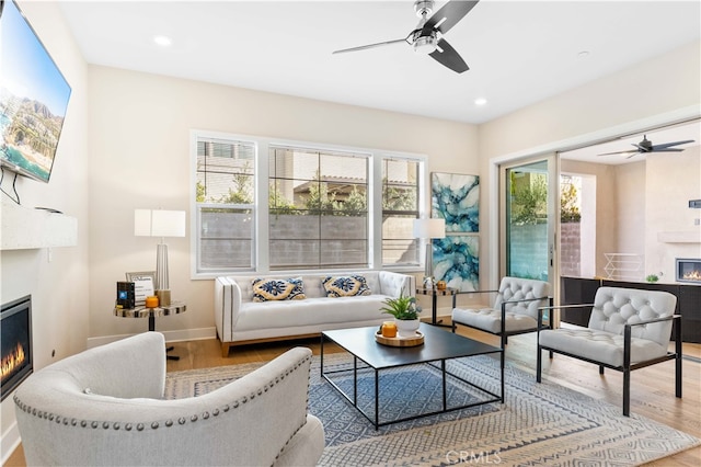 living room featuring ceiling fan, a large fireplace, and hardwood / wood-style flooring