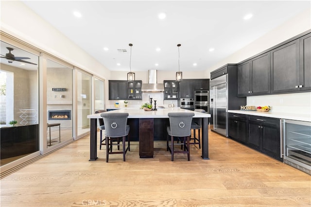 kitchen with a center island, pendant lighting, a kitchen bar, light hardwood / wood-style flooring, and wall chimney range hood