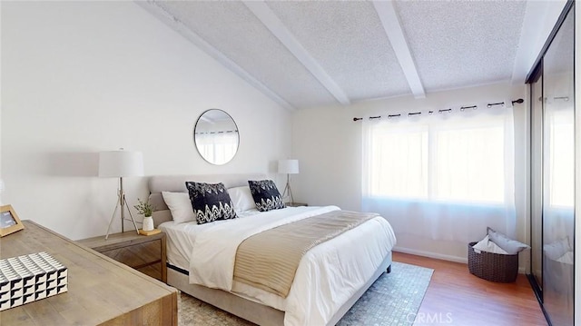 bedroom with hardwood / wood-style flooring, a textured ceiling, and lofted ceiling with beams