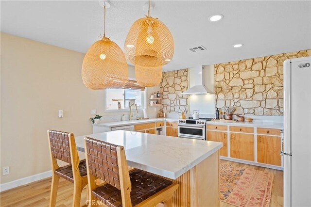 kitchen featuring range with two ovens, pendant lighting, wall chimney range hood, white refrigerator, and sink