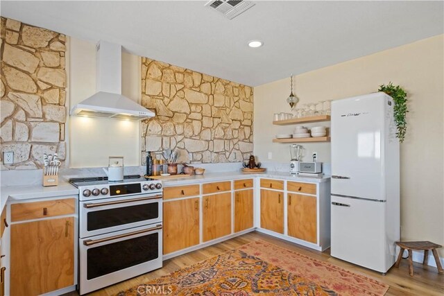 kitchen with light wood-type flooring, white refrigerator, wall chimney exhaust hood, and double oven range