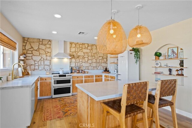 kitchen featuring range with two ovens, wall chimney exhaust hood, light wood-type flooring, white refrigerator, and sink