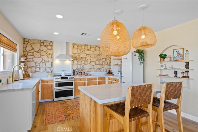 kitchen featuring sink, double oven range, white fridge, light hardwood / wood-style floors, and wall chimney range hood