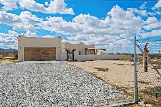 pueblo revival-style home with a garage, gravel driveway, fence, and stucco siding