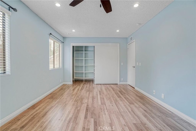 unfurnished bedroom with light wood-type flooring, a textured ceiling, ceiling fan, and a closet