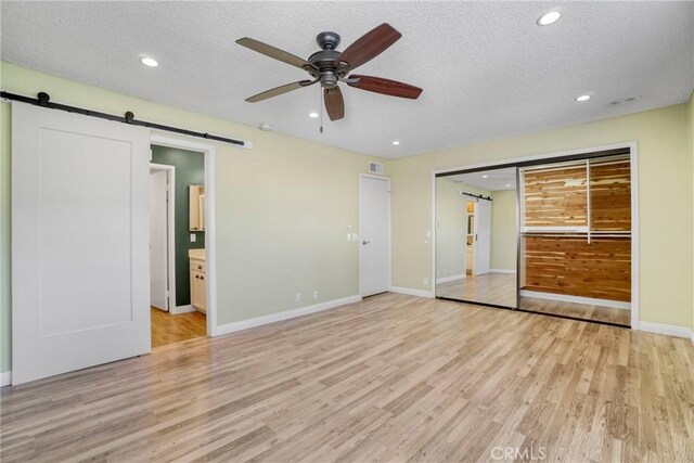 unfurnished bedroom with a closet, light hardwood / wood-style floors, connected bathroom, a barn door, and ceiling fan