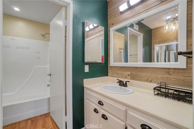 bathroom featuring vanity, wood walls, hardwood / wood-style floors, and tub / shower combination