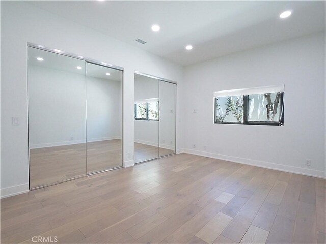 unfurnished bedroom featuring multiple closets and light wood-type flooring