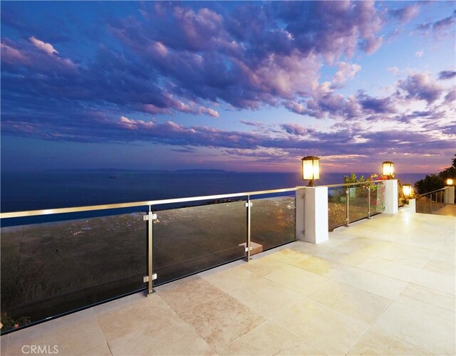 balcony at dusk featuring a water view