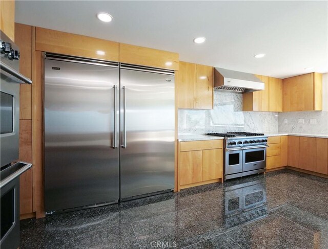 kitchen with high quality appliances, wall chimney range hood, tasteful backsplash, and light brown cabinets