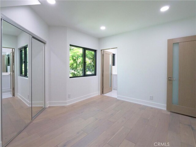 unfurnished bedroom featuring ensuite bathroom and light hardwood / wood-style flooring