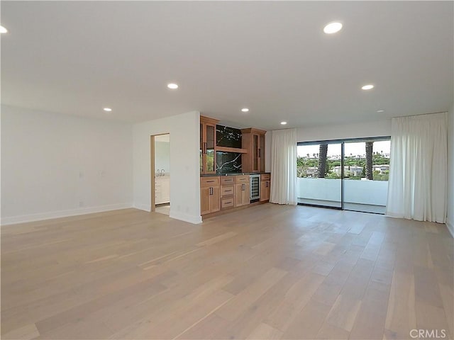 unfurnished living room featuring beverage cooler and light hardwood / wood-style floors