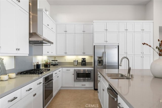 kitchen featuring white cabinets, wall chimney range hood, stainless steel appliances, and a sink