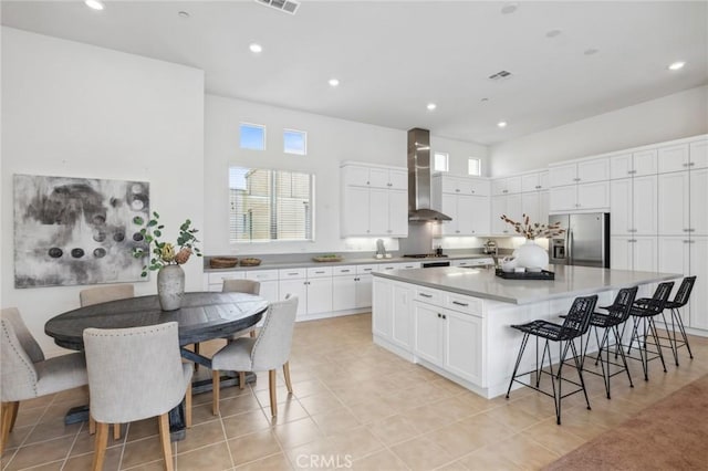 kitchen with a breakfast bar area, a sink, white cabinets, appliances with stainless steel finishes, and wall chimney range hood