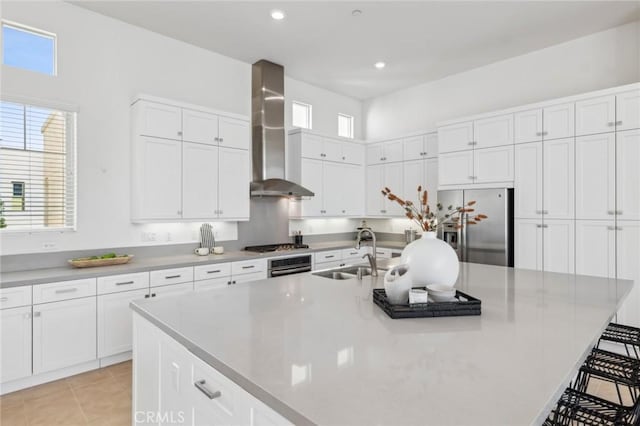 kitchen with light tile patterned floors, stainless steel appliances, white cabinetry, a sink, and wall chimney range hood