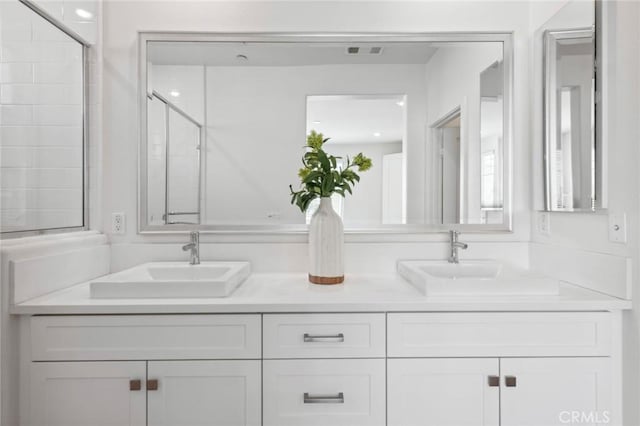 bathroom featuring double vanity, visible vents, a sink, and tiled shower