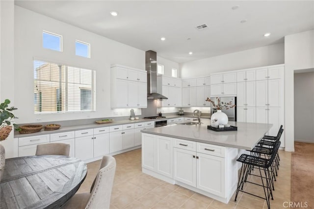 kitchen with visible vents, white cabinets, wall chimney exhaust hood, appliances with stainless steel finishes, and a sink