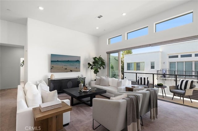 carpeted living area with recessed lighting, visible vents, and a high ceiling