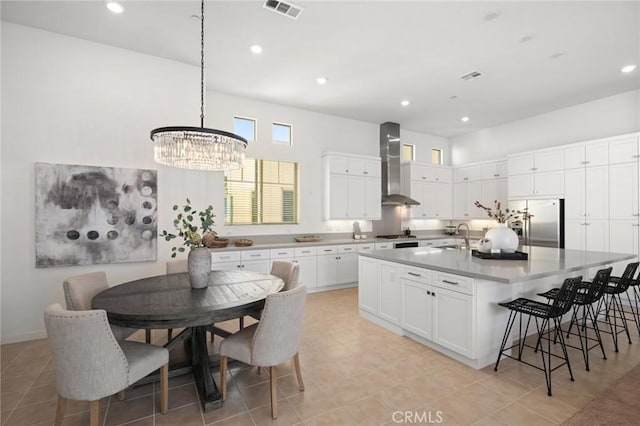 kitchen featuring stainless steel appliances, visible vents, white cabinets, wall chimney exhaust hood, and a large island with sink