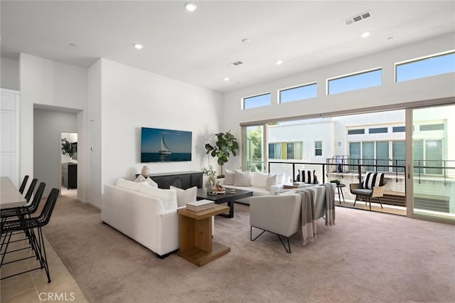 living area with a towering ceiling, light carpet, visible vents, and recessed lighting