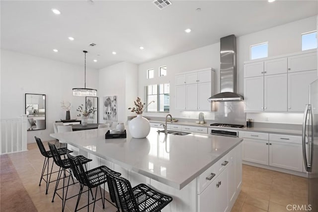 kitchen with visible vents, a spacious island, wall chimney exhaust hood, stainless steel gas stovetop, and a sink