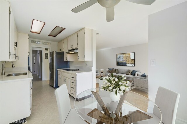 kitchen featuring stainless steel refrigerator, ceiling fan, black electric cooktop, sink, and white cabinetry