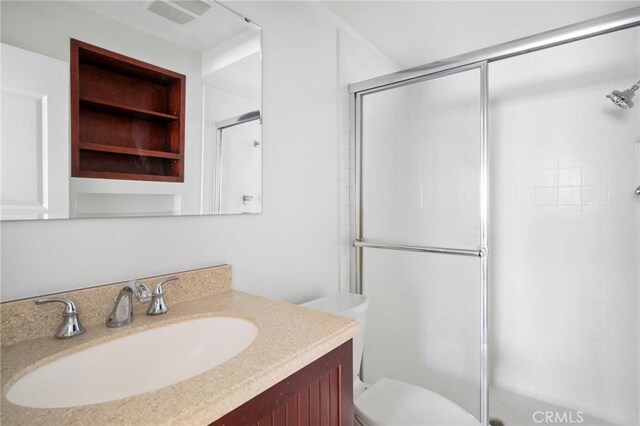 bathroom featuring toilet, built in features, a shower with shower door, and vanity