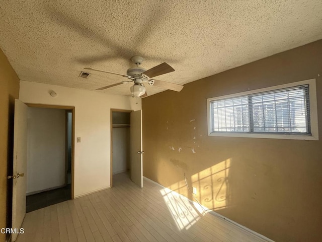 unfurnished bedroom featuring light wood-type flooring, ceiling fan, a closet, and a textured ceiling