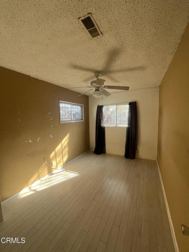 spare room featuring light wood-type flooring, ceiling fan, and a textured ceiling