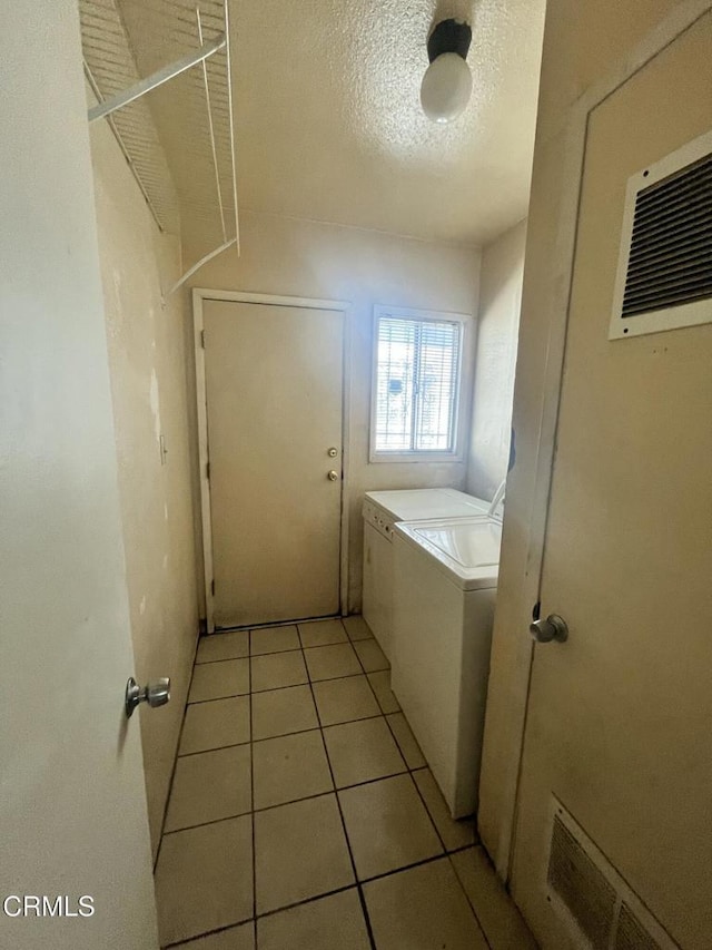 clothes washing area with independent washer and dryer, a textured ceiling, and light tile patterned floors