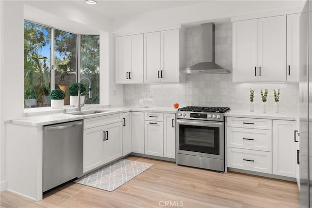 kitchen with sink, stainless steel appliances, white cabinetry, and wall chimney range hood