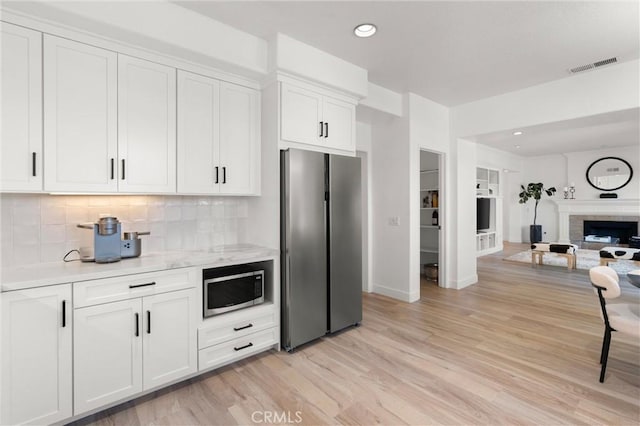 kitchen with stainless steel appliances, light stone countertops, white cabinets, light hardwood / wood-style flooring, and backsplash