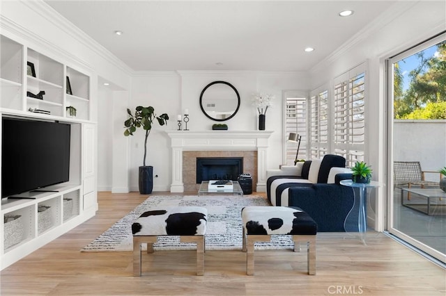 living room featuring a tiled fireplace, light wood-type flooring, and ornamental molding