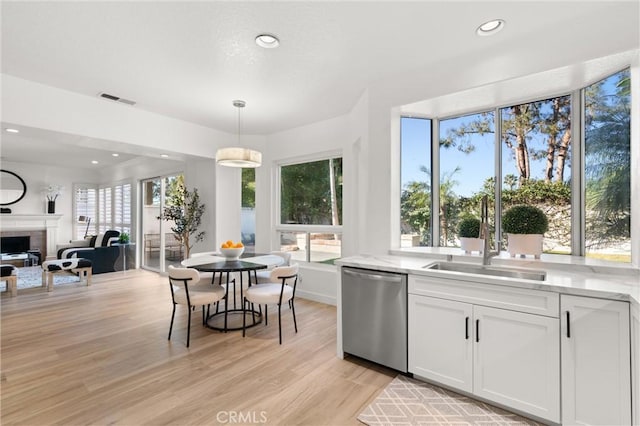 kitchen with sink, white cabinets, light hardwood / wood-style floors, stainless steel dishwasher, and hanging light fixtures