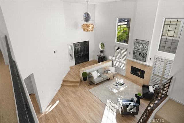 living room featuring a towering ceiling, light wood-type flooring, a tiled fireplace, and a healthy amount of sunlight