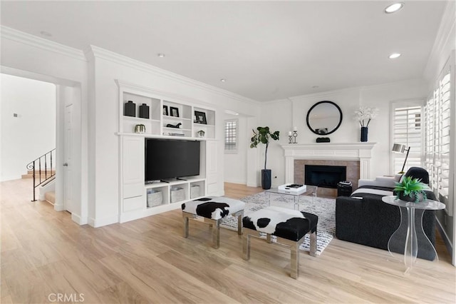 living room featuring light hardwood / wood-style flooring, a tile fireplace, and crown molding