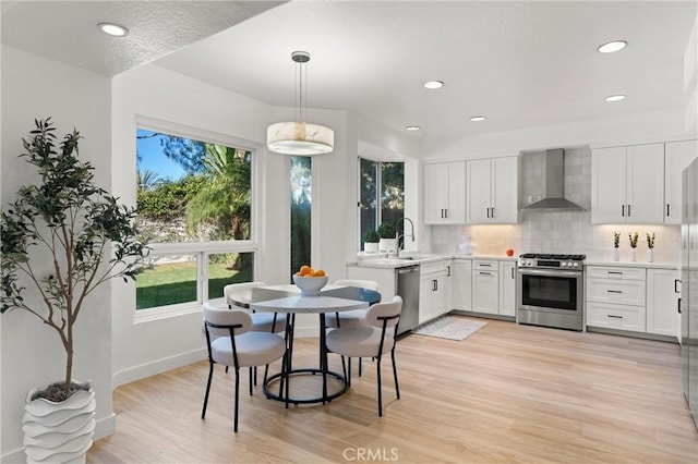 kitchen with stainless steel appliances, white cabinets, decorative light fixtures, wall chimney exhaust hood, and decorative backsplash