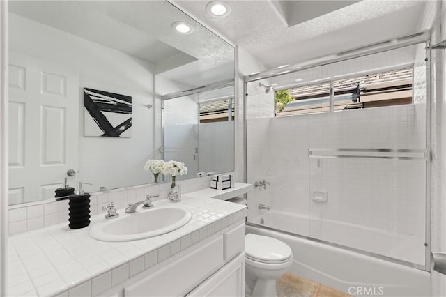 full bathroom featuring toilet, bath / shower combo with glass door, a textured ceiling, and vanity