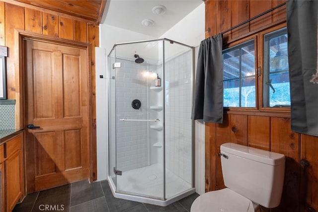 bathroom featuring toilet, wooden walls, tile patterned flooring, and walk in shower