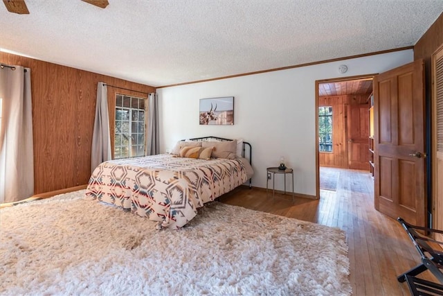 bedroom featuring wooden walls, a textured ceiling, hardwood / wood-style floors, ceiling fan, and ornamental molding