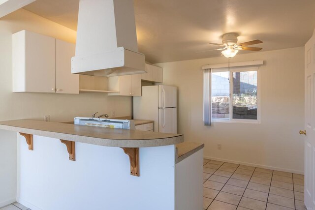 kitchen featuring white cabinets, a kitchen bar, white fridge, and island exhaust hood