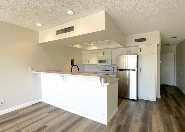 kitchen featuring white appliances, kitchen peninsula, a textured ceiling, dark wood-type flooring, and white cabinets