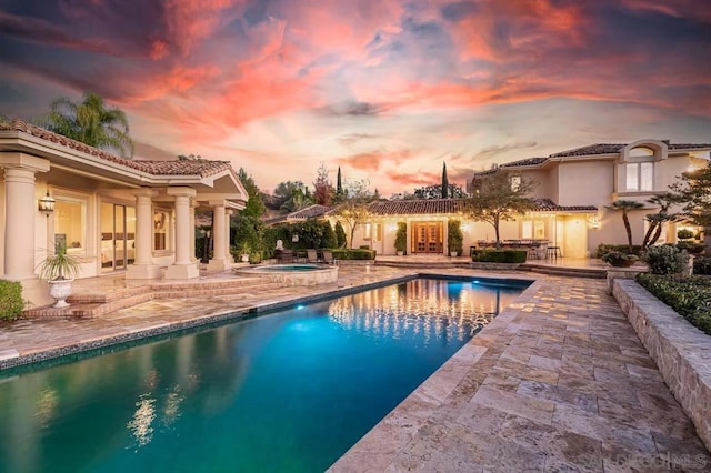 pool at dusk featuring a patio and an in ground hot tub