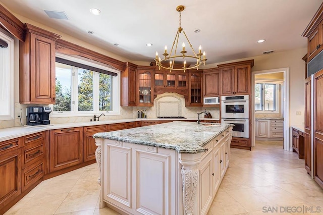 kitchen featuring appliances with stainless steel finishes, an island with sink, light stone countertops, an inviting chandelier, and decorative light fixtures