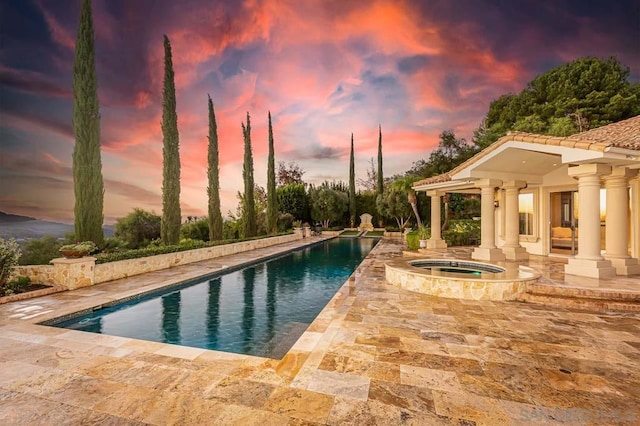 pool at dusk with an in ground hot tub and a patio