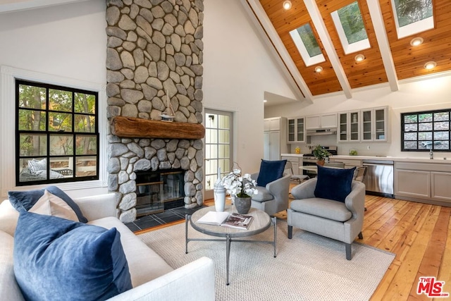 living room with a stone fireplace, wooden ceiling, a skylight, high vaulted ceiling, and beam ceiling