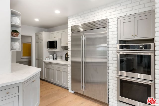 kitchen featuring stainless steel appliances, light wood-type flooring, light stone countertops, and gray cabinets