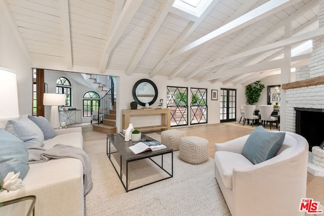 living room with light hardwood / wood-style floors, a healthy amount of sunlight, a brick fireplace, and vaulted ceiling with beams