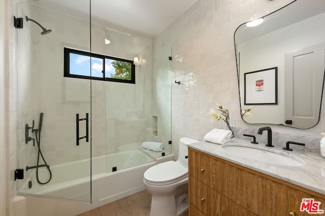 full bathroom with tile walls, toilet, wood-type flooring, bath / shower combo with glass door, and vanity